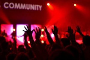 Many people are in a crowd with their hands up in the air facing the stage. The banner above the stage reads, "Community".