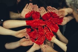 Several people holding their hands out together in a group with a heart painted across them.