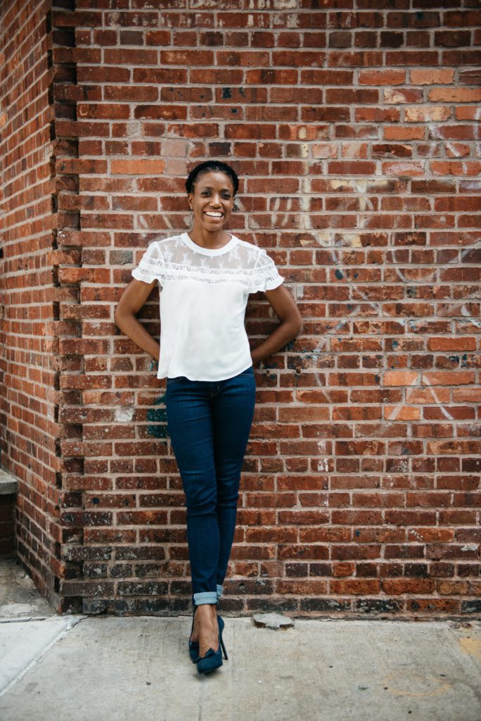 Marie Deveaux is leaning against the brick wall outside a local store.